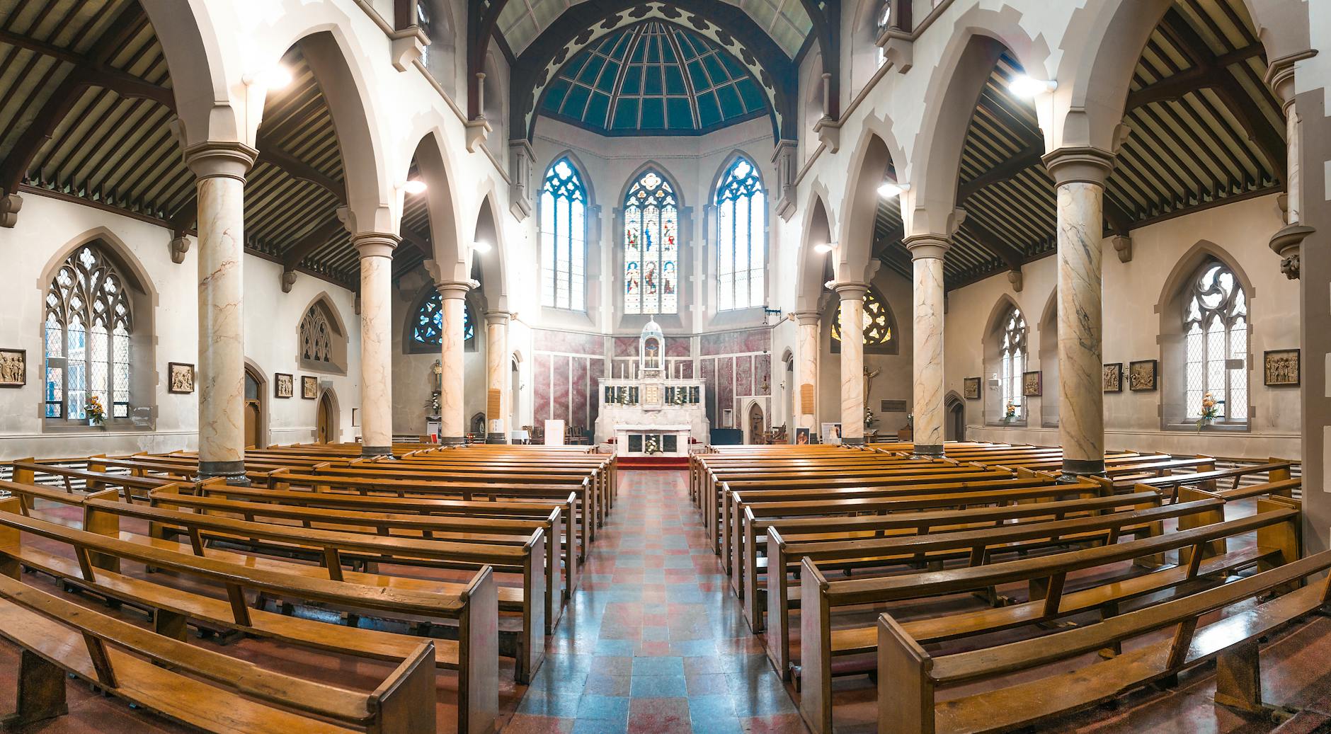 Wnętrze zabytkowego kościoła z kolorowymi witrażami i drewnianymi ławami