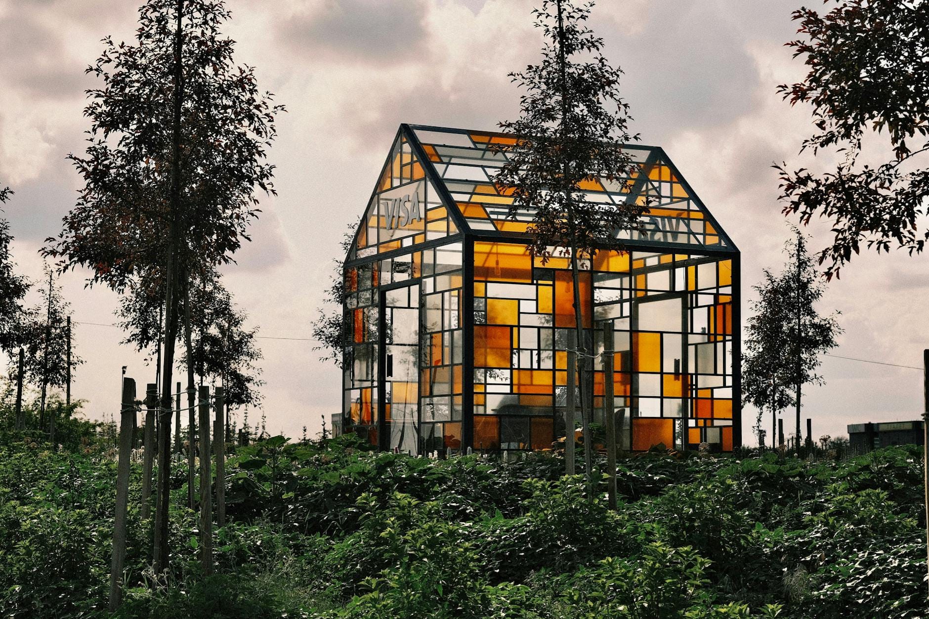 Kolorowy szklany dom wśród zieleni na tle ogrodu