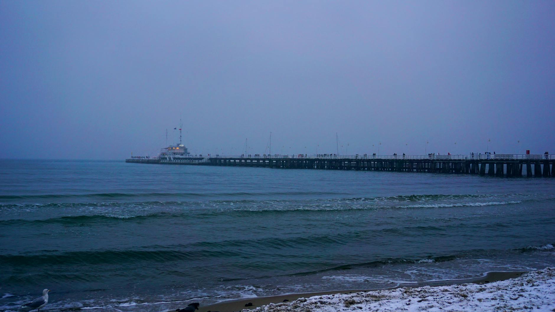 Molo w Sopocie zimą o zmierzchu nad spokojnym, lekko falującym morzem